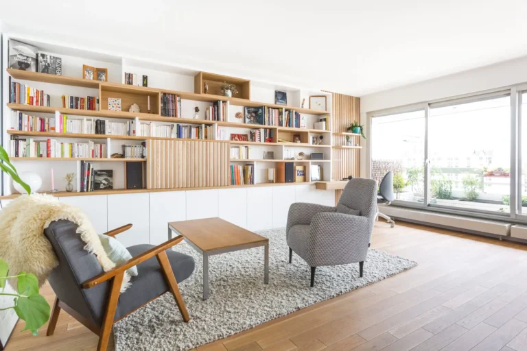 Grande bibliothèque sur mesure avec bureau intégré en bois clair et blanc laqué dans un salon lumineux