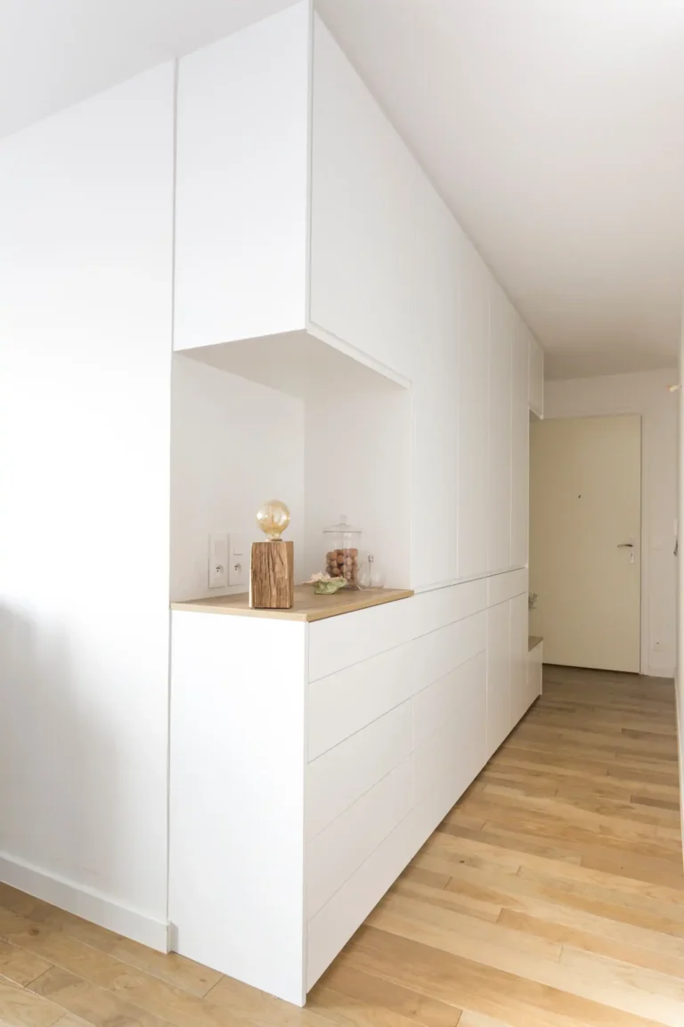 Meuble d’entrée blanc toute hauteur avec niche bois clair dans un couloir étroit